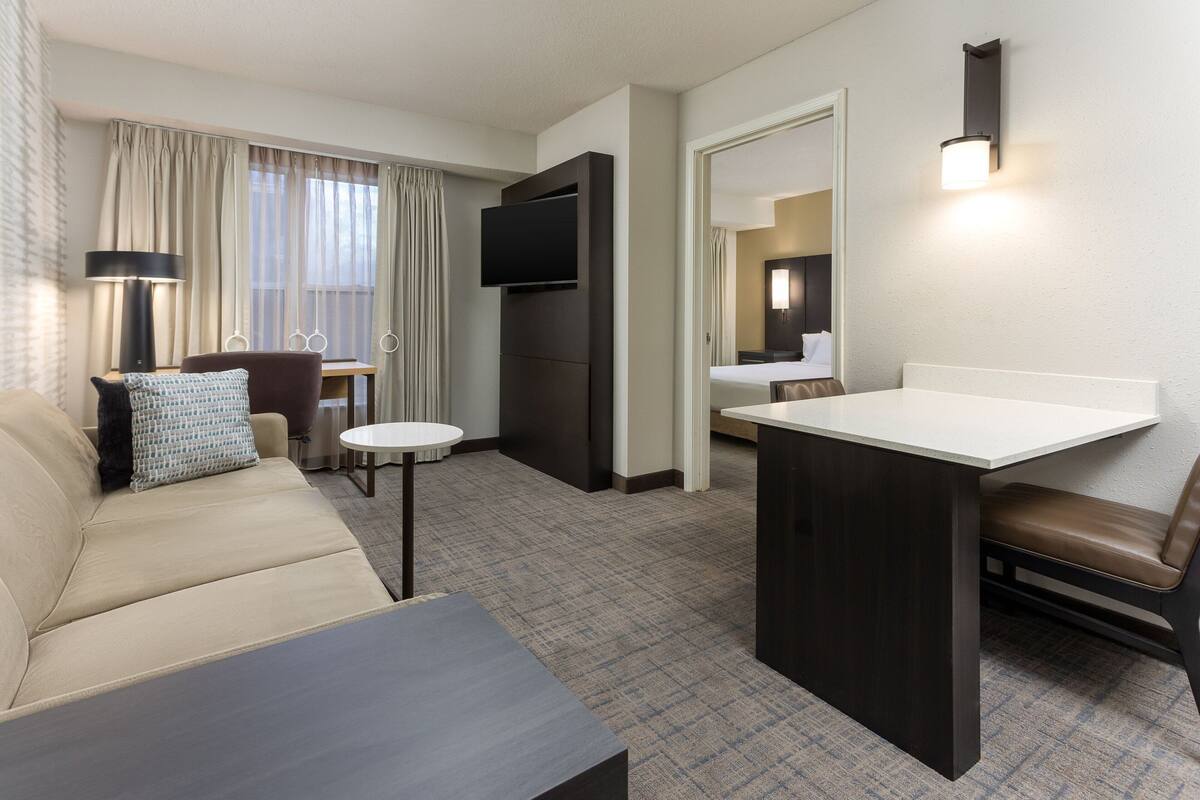 A hotel room with a sofa, a small table, a TV, a desk, and a chair.