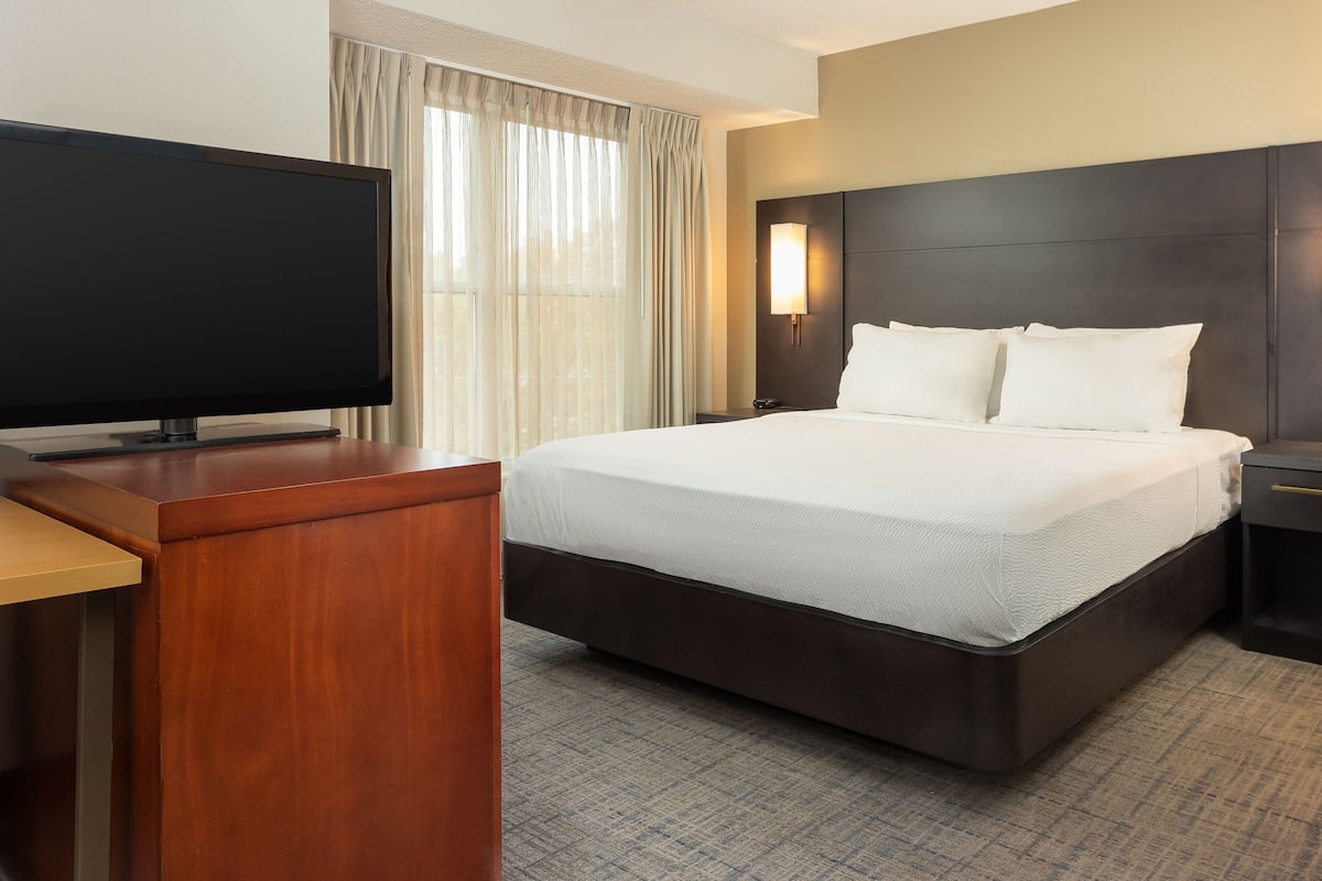 A hotel room with a bed, a TV, a nightstand, and a window with curtains.