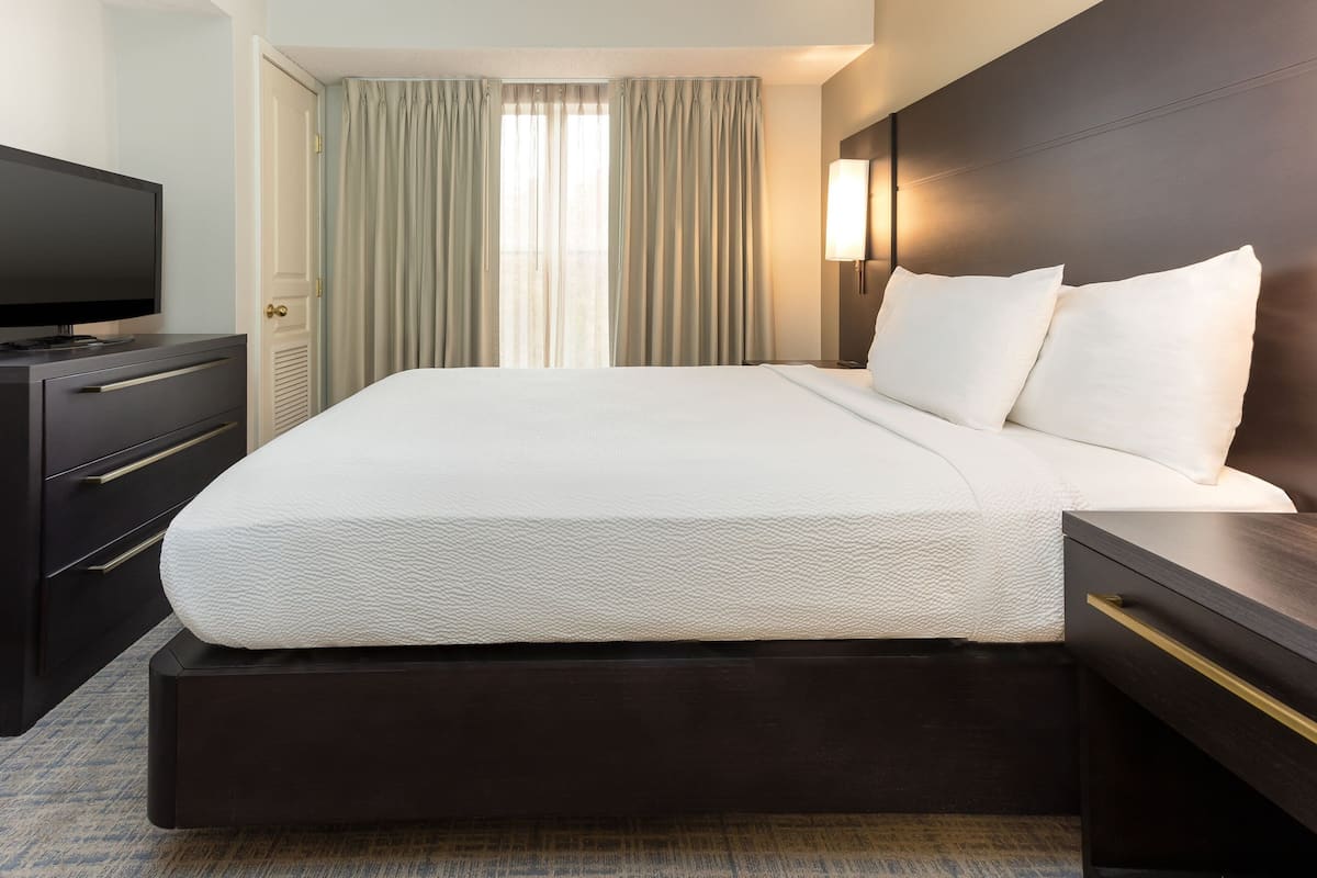 A hotel room with a bed, a TV, a nightstand, and a window with curtains.