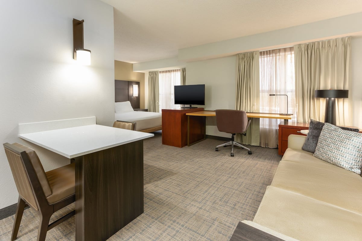 A hotel room with a bed, desk, chair, TV, and a small kitchenette area.