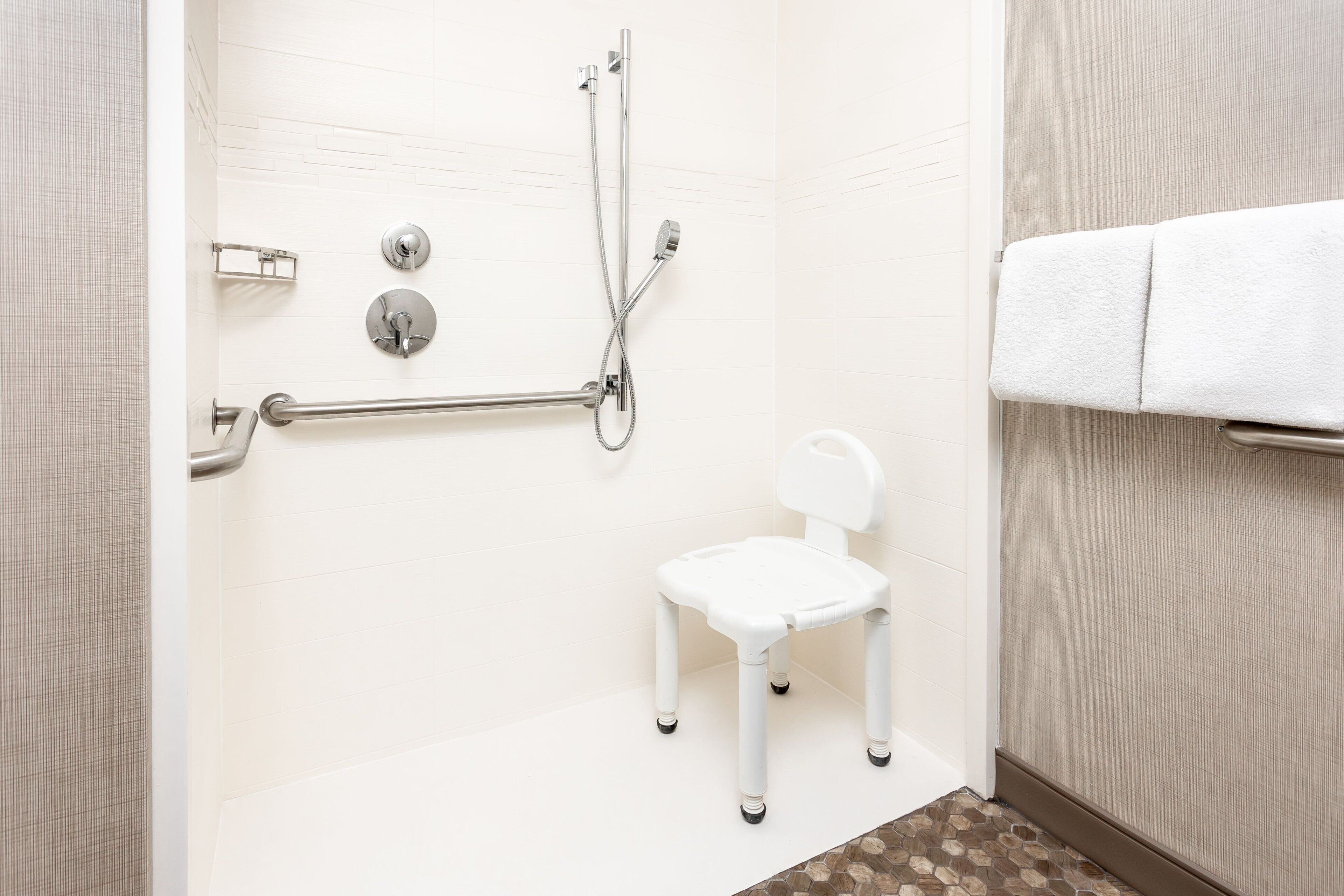 A bathroom with a white shower, a white chair, and a towel rack.