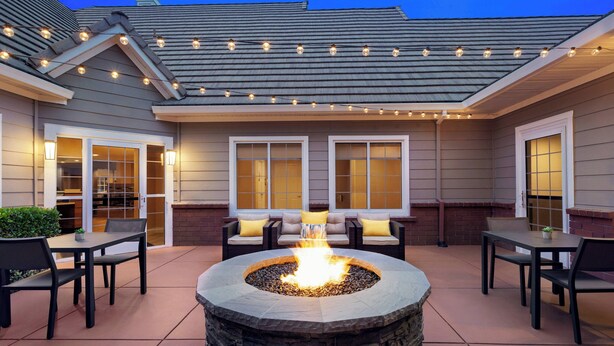 An outdoor patio with a stone fire pit, seating, and string lights. - Residence Inn by Marriott Vacaville (Vacaville)