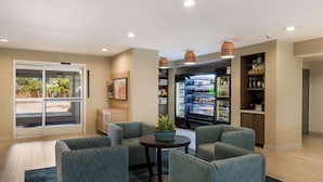Uma área de estar moderna, com assentos, um refrigerador repleto de bebidas e vista através de uma porta de vidro.