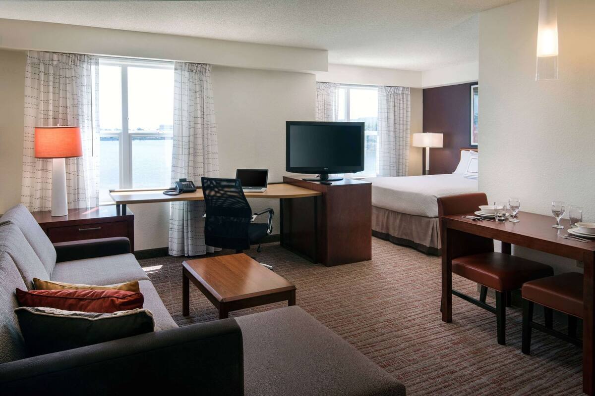 A hotel room with a bed, a desk with a computer, a television, a sofa, and a dining table.