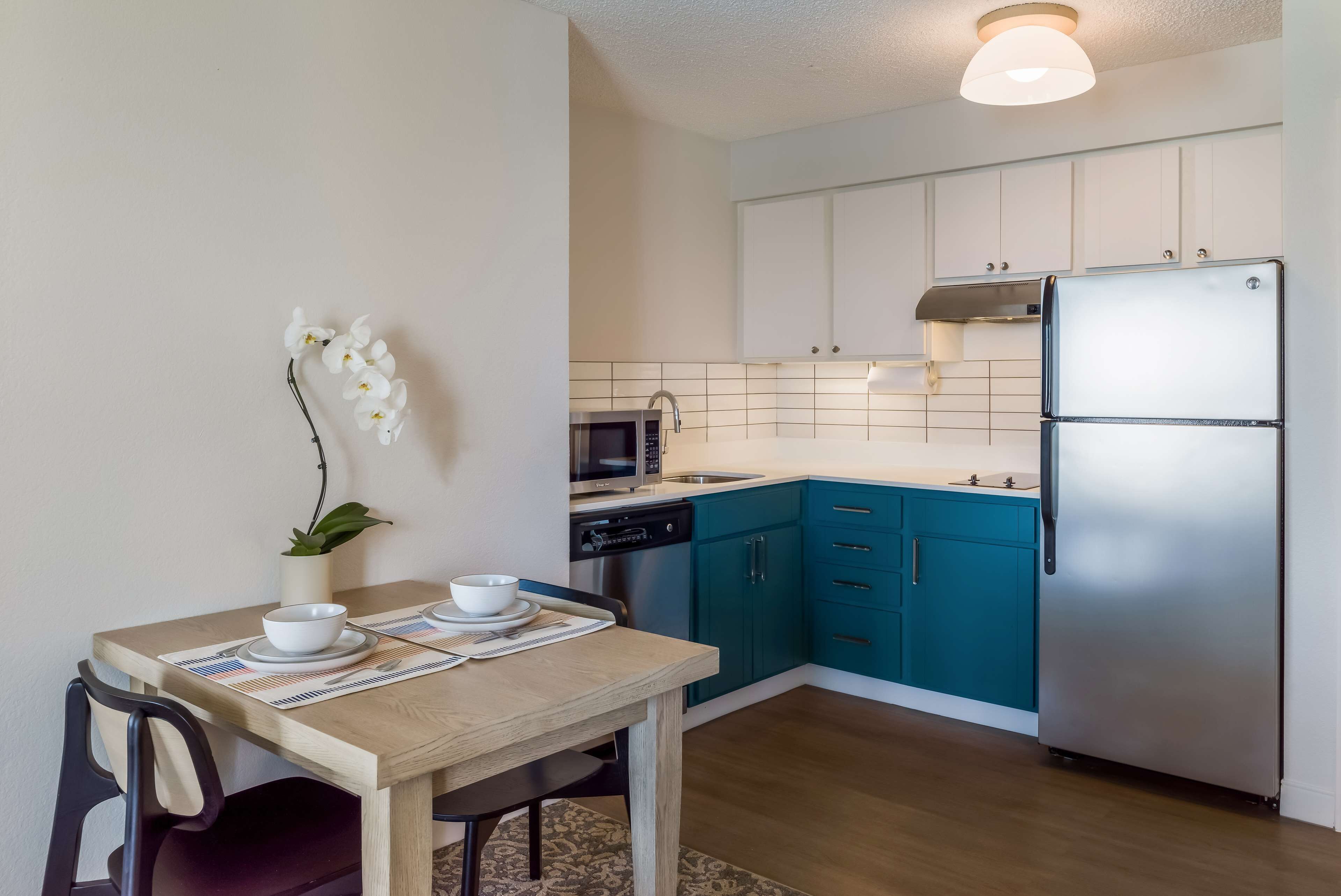 A modern kitchen with teal cabinets, a stainless steel refrigerator, and a microwave.