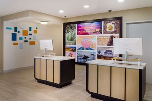 A reception area with two reception desks, a wall with abstract art, and a large poster with various images. - Sonesta ES Suites San Francisco Airport Oyster Point Waterfront (South San Francisco)