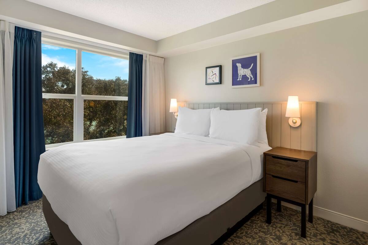 A hotel room with a large bed, two wall-mounted lamps, and a window with curtains.