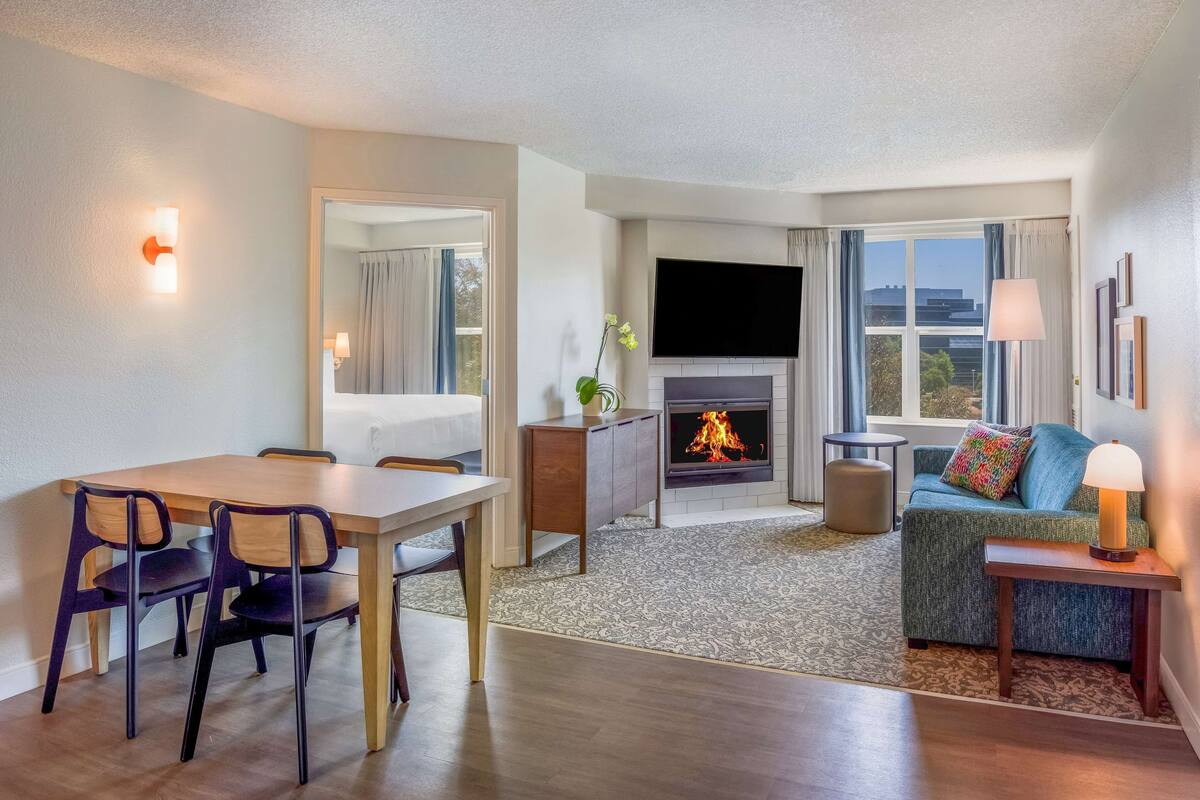 A modern living room with a fireplace, a TV, a sofa, and a dining area with chairs.