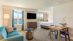 Quarto de hotel com sofá, mesa redonda pequena, cama, televisão e mesa de jantar com cadeiras.