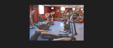 Un gimnasio con varias máquinas de ejercicio, incluyendo cintas de correr y máquinas elípticas, dispuestas en filas.
