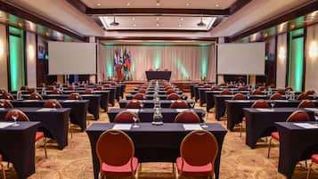 A conference room with rows of tables and chairs, a stage with a podium, and flags.