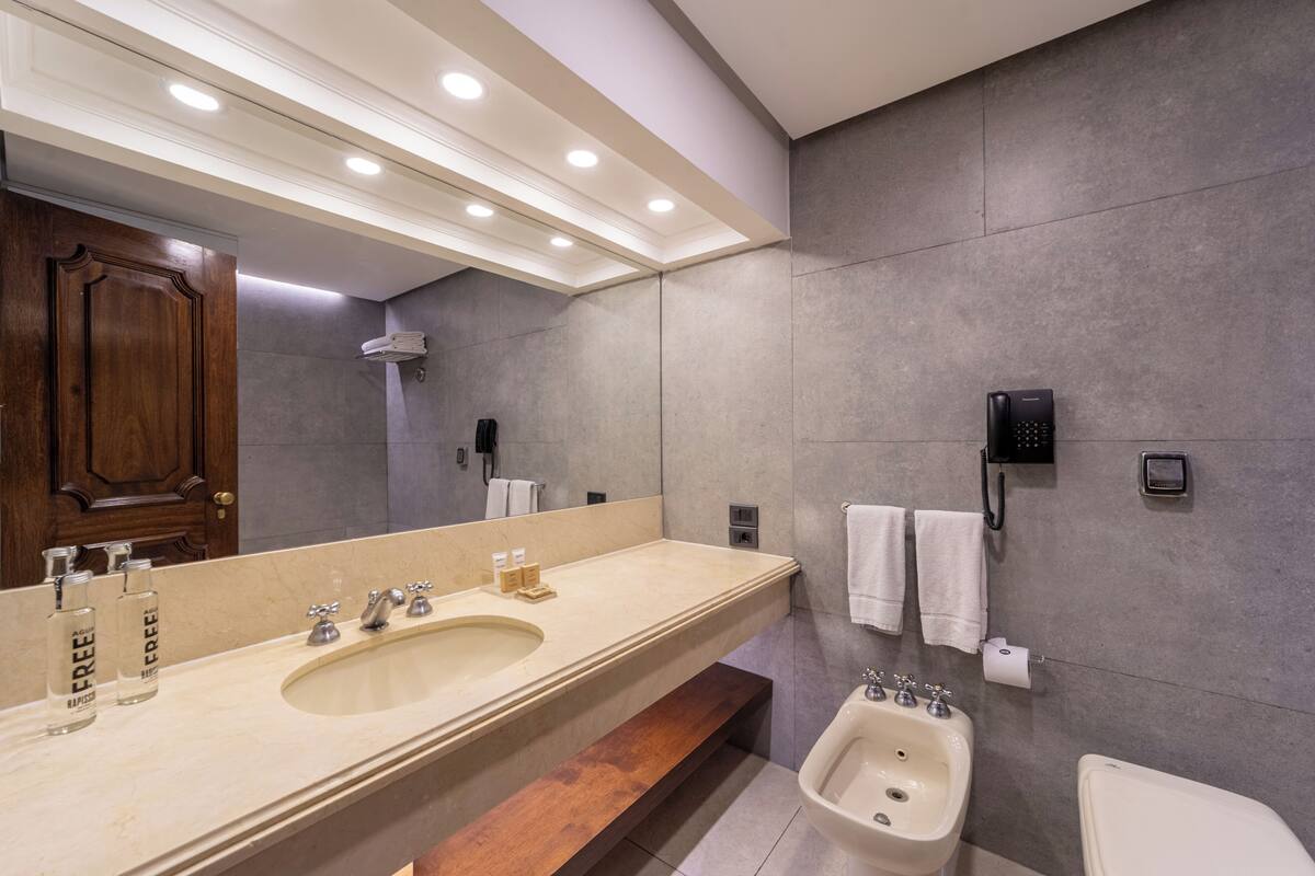 Ein modernes Badezimmer mit großem Spiegel, zwei Waschbecken, einem Bidet und einer Toilette.