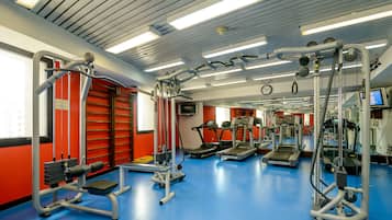 Uma academia com esteiras, aparelhos de musculação e piso azul.
