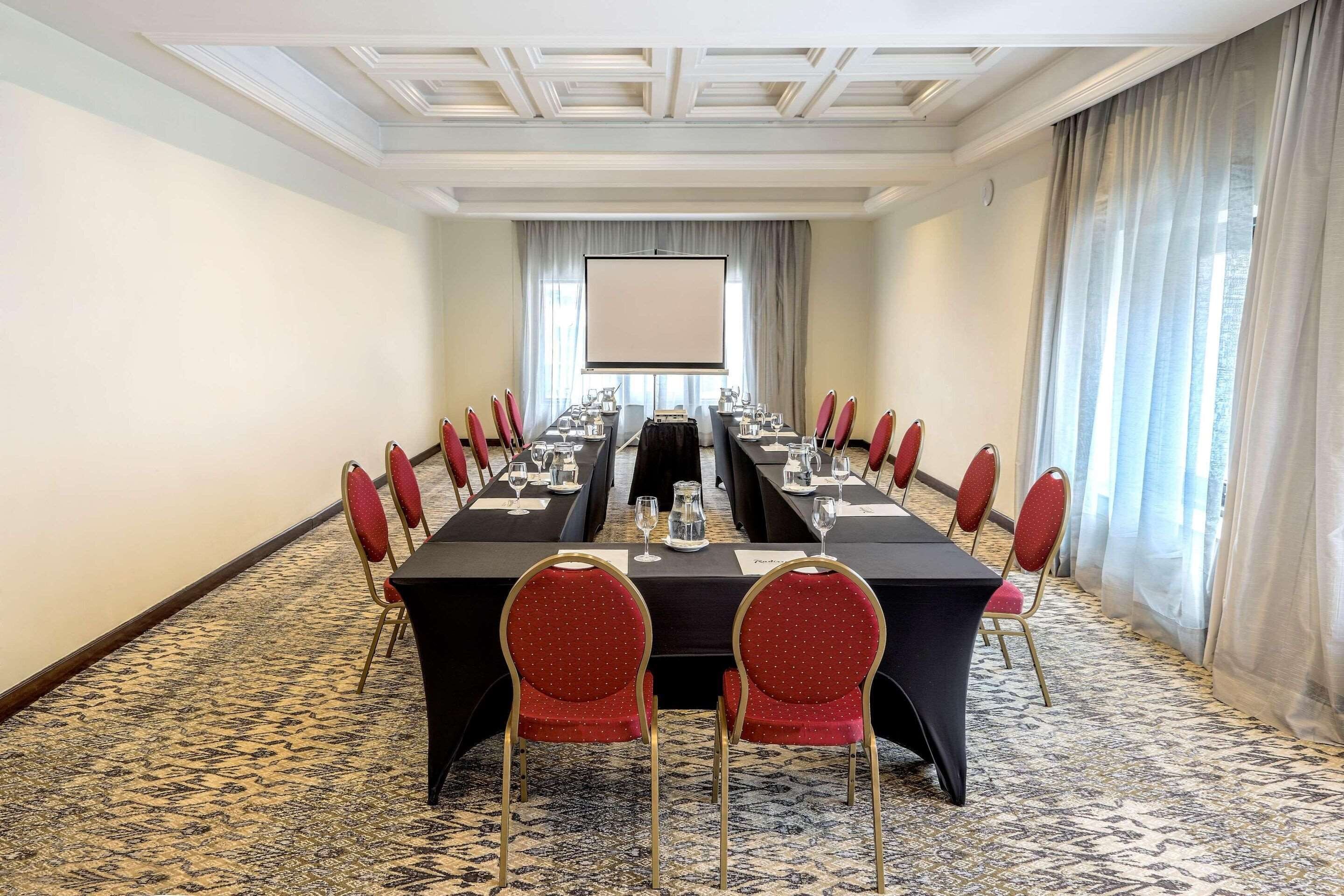 A conference room with a long table, red chairs, and a projector screen.