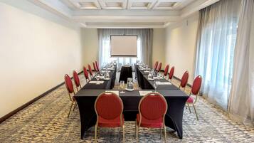 A conference room with a long table, red chairs, and a projector screen.