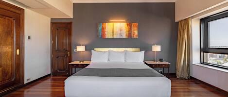 A hotel room with a large bed, two bedside tables, a nightstand, a window with a view, and a door.