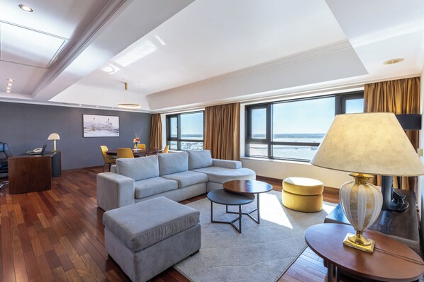 A modern living room with a sectional sofa, ottoman, round coffee table, and a lamp. - Radisson Montevideo Victoria Plaza Hotel (Montevideo)