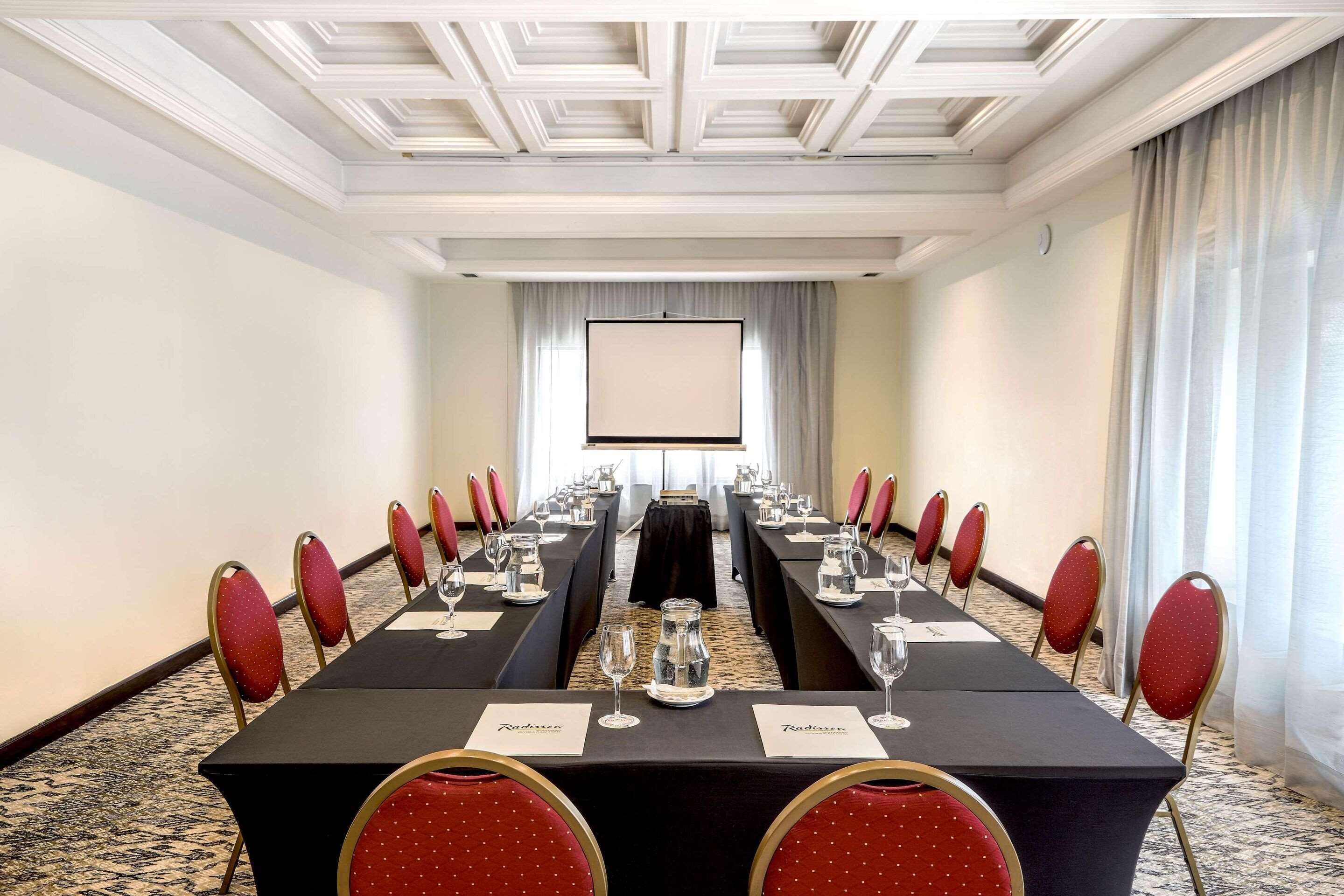 Ein Konferenzraum mit einem langen Tisch, roten Stühlen, Namensschildern und einer Projektionsleinwand.