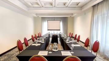 Ein Konferenzraum mit einem langen Tisch, roten Stühlen, Namensschildern und einer Projektionsleinwand.