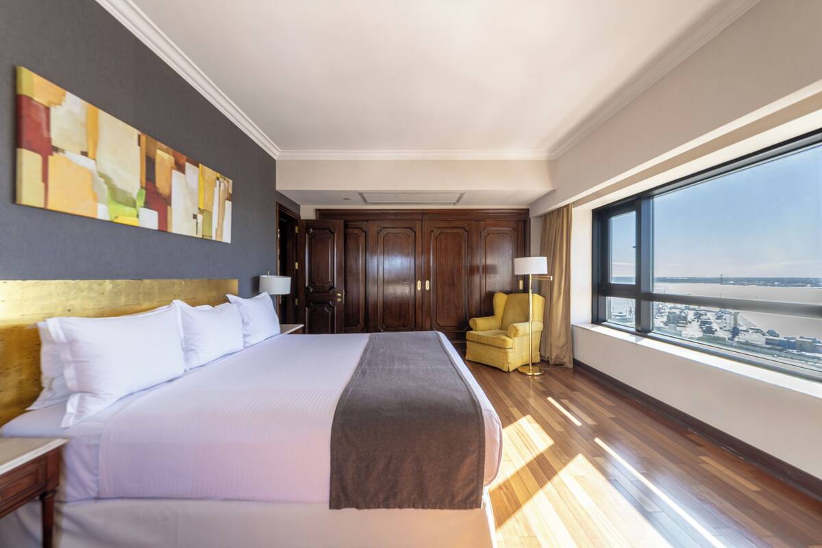 Ein Hotelzimmer mit einem großen Bett, Blick auf die Stadt und Holzboden.