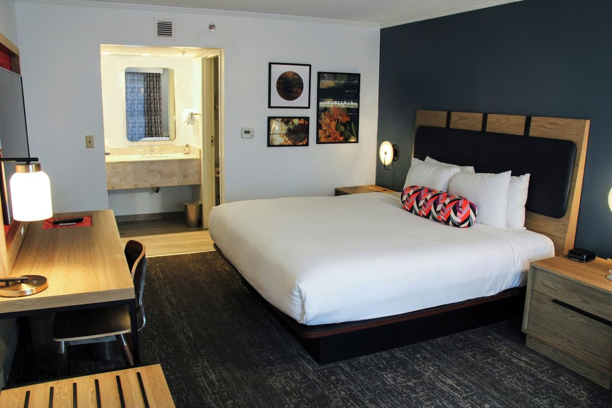 Hotelkamer met een bed, nachtkastje, bureau, stoel en een badkamer zichtbaar door een geopende deur.