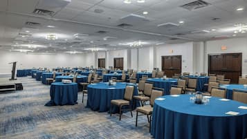 A conference room with round tables covered in blue tablecloths, arranged in rows.