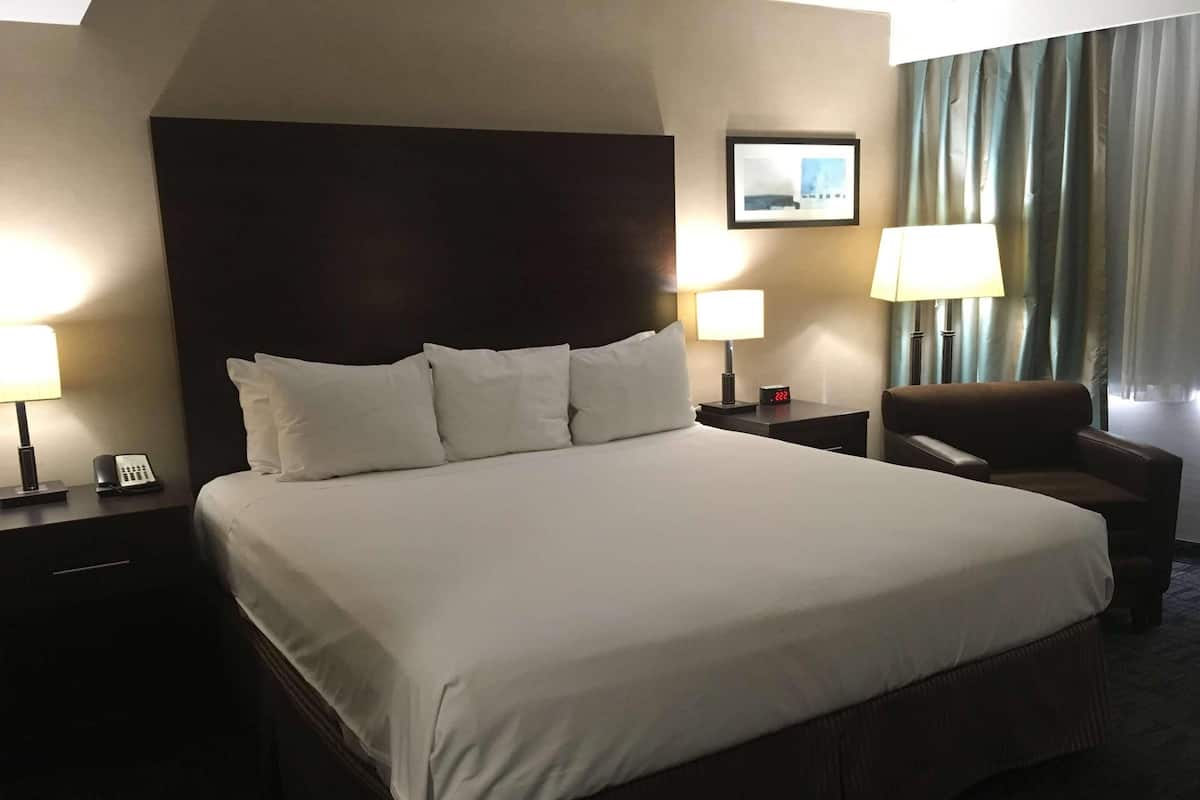 Ein Hotelzimmer mit einem großen Bett, zwei Nachttischen, einem Sessel und einem Wandbild.