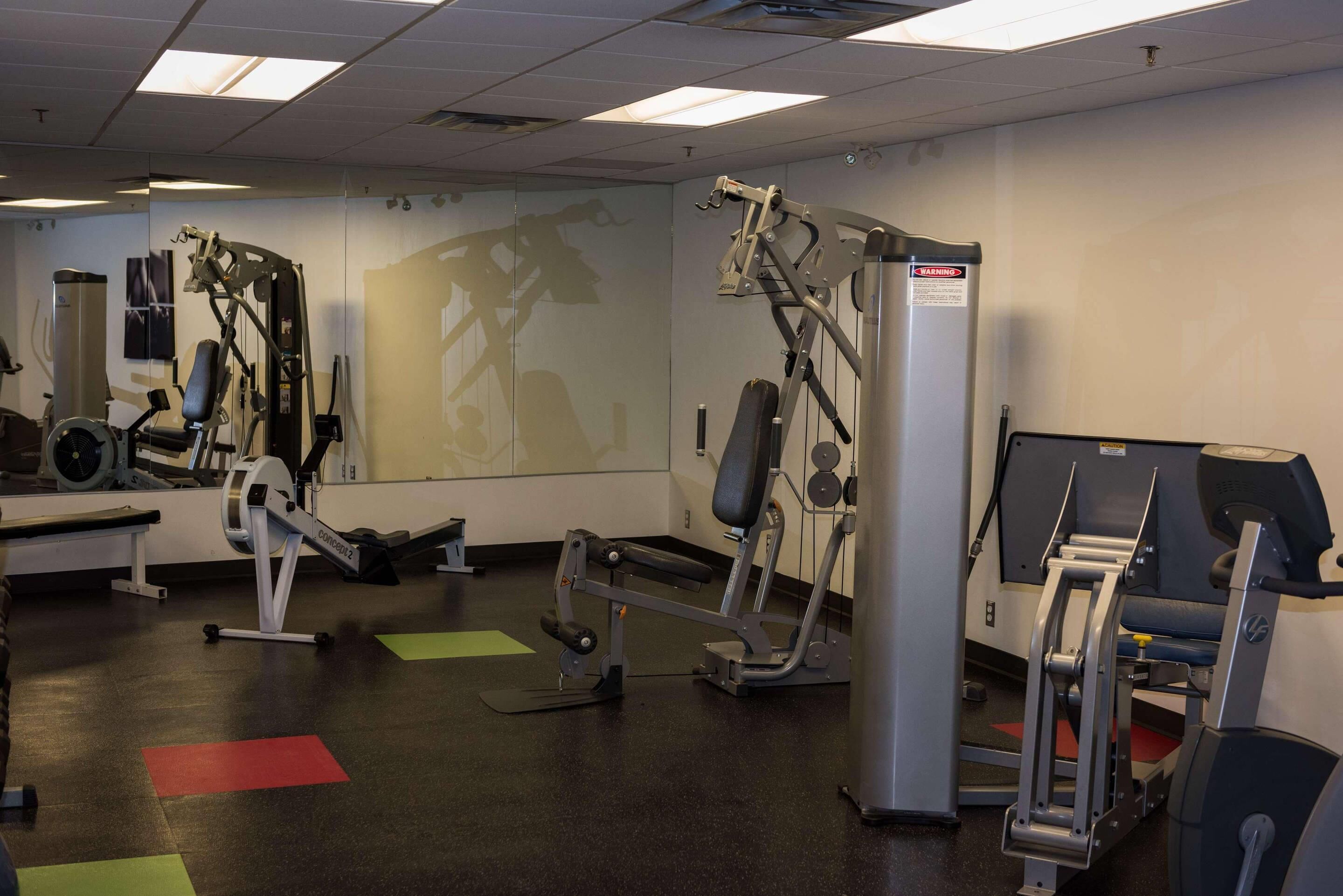 A gym with various exercise machines, a bench, and a mirror on the wall.