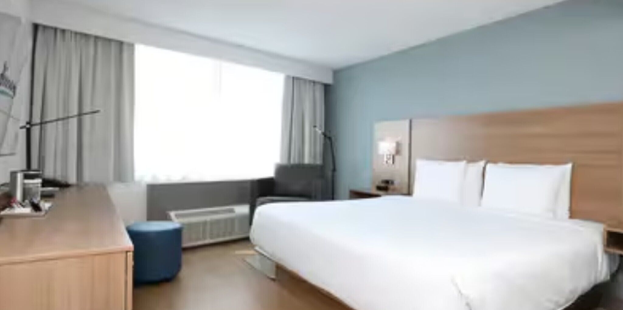 A hotel room with a large bed, a desk, a chair, a small table, and a window with curtains.