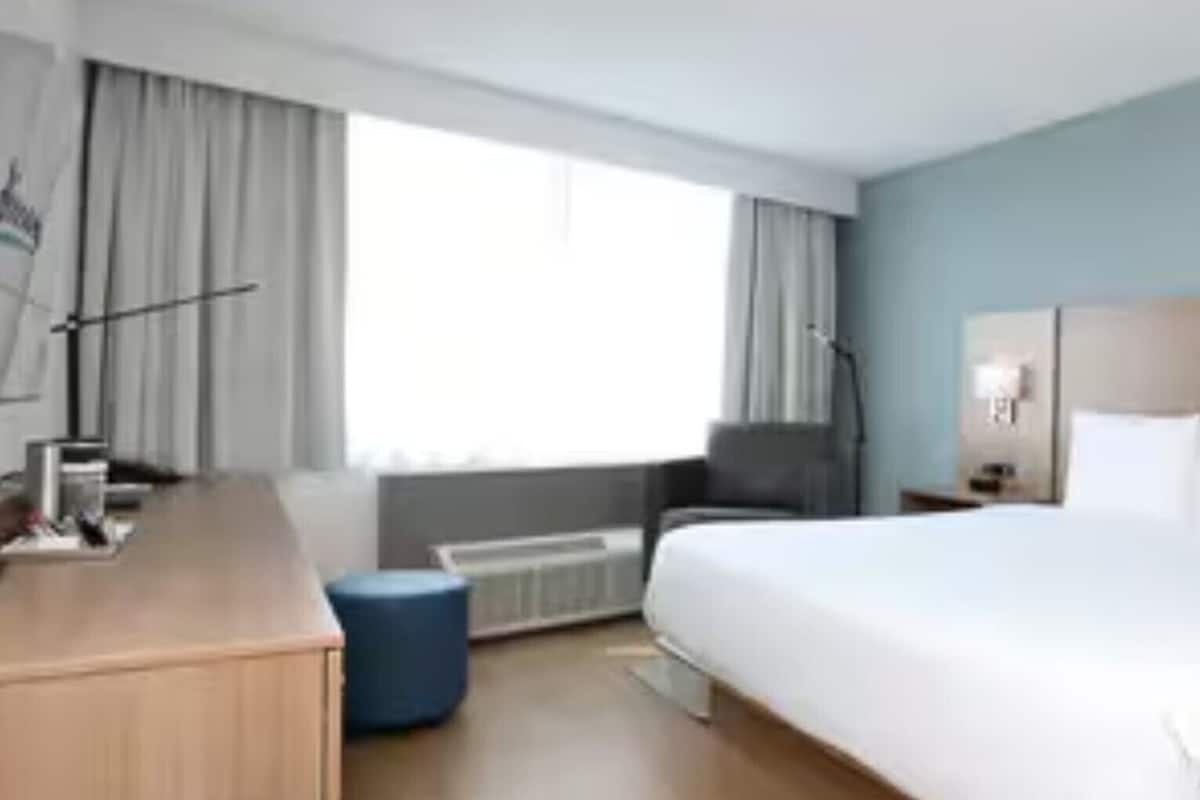 A hotel room with a large bed, a desk, a chair, a small table, and a window with curtains.