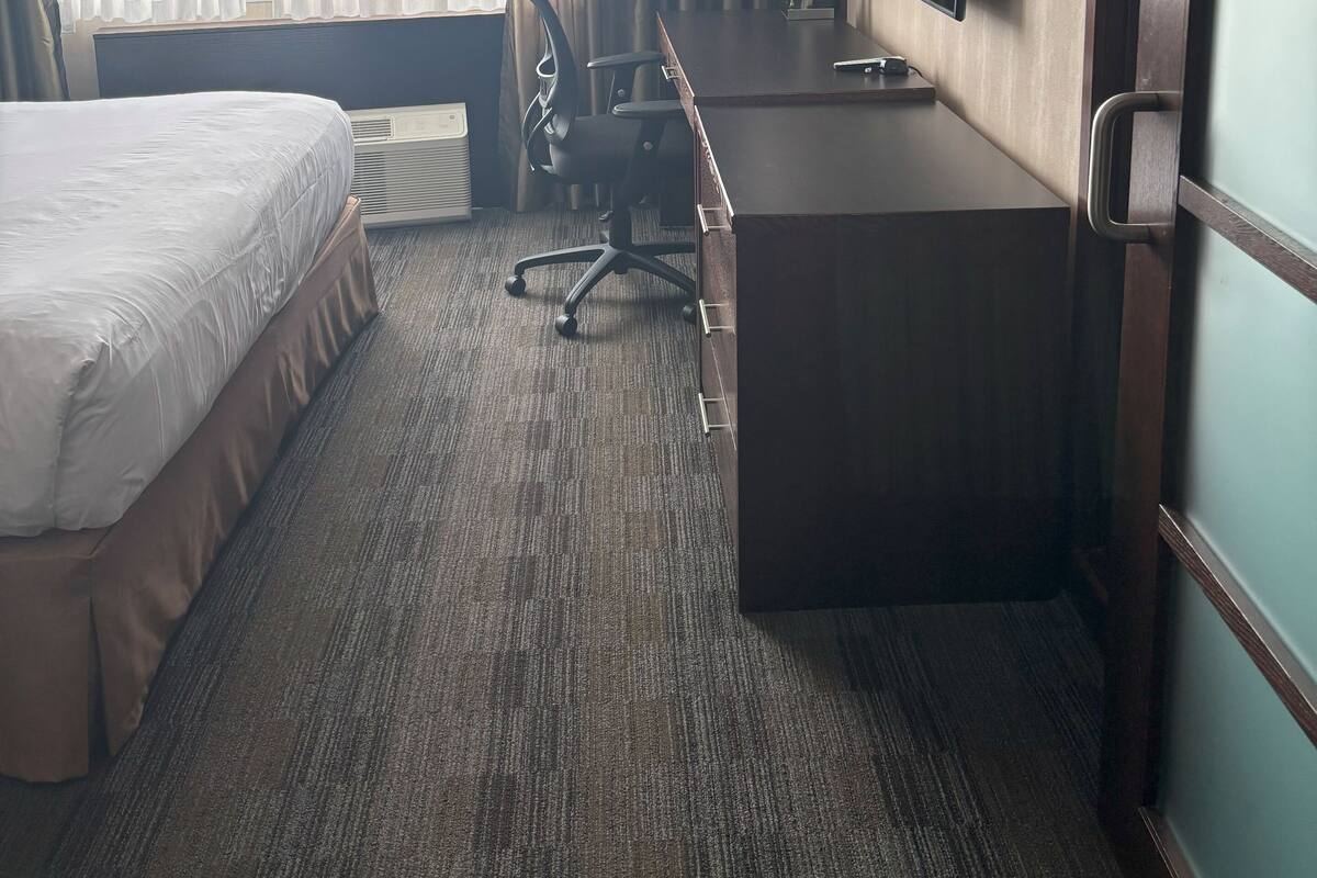 Ein Hotelzimmer mit Bett, Schreibtisch, Stuhl und einem großen Fenster mit Vorhängen.