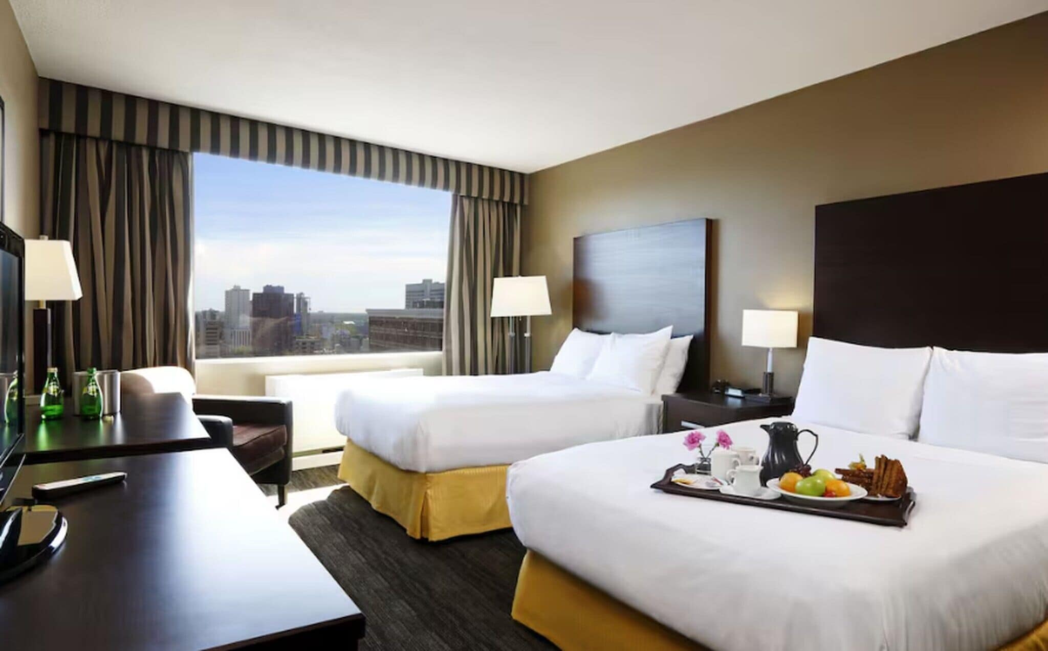 A hotel room with two beds, a desk, a chair, a TV, and a city view.