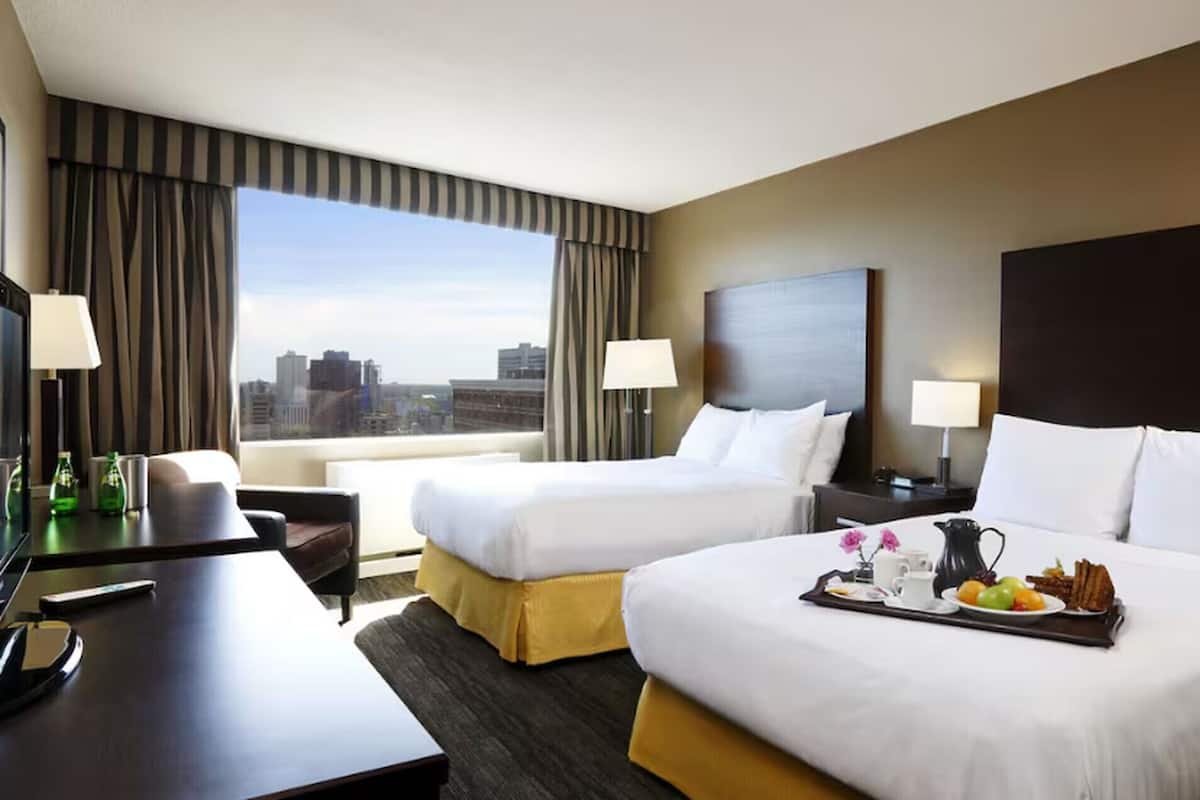 A hotel room with two beds, a desk, a chair, a TV, and a city view.