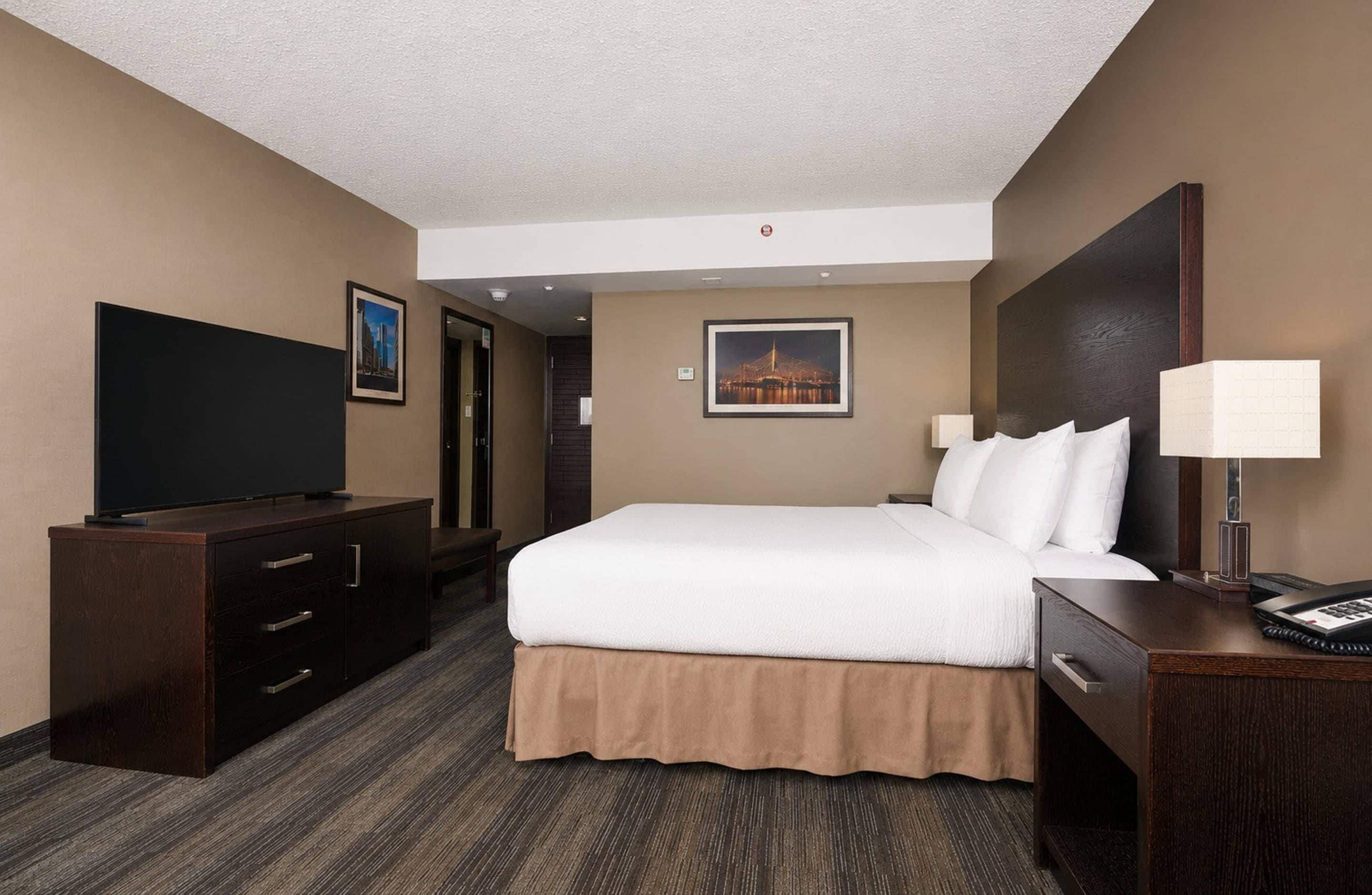 A hotel room with a bed, a TV, a desk with a lamp, and a picture on the wall.