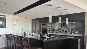 Una zona de bar moderna con una barra larga, varios taburetes y una estantería bien surtida con diferentes botellas y copas.