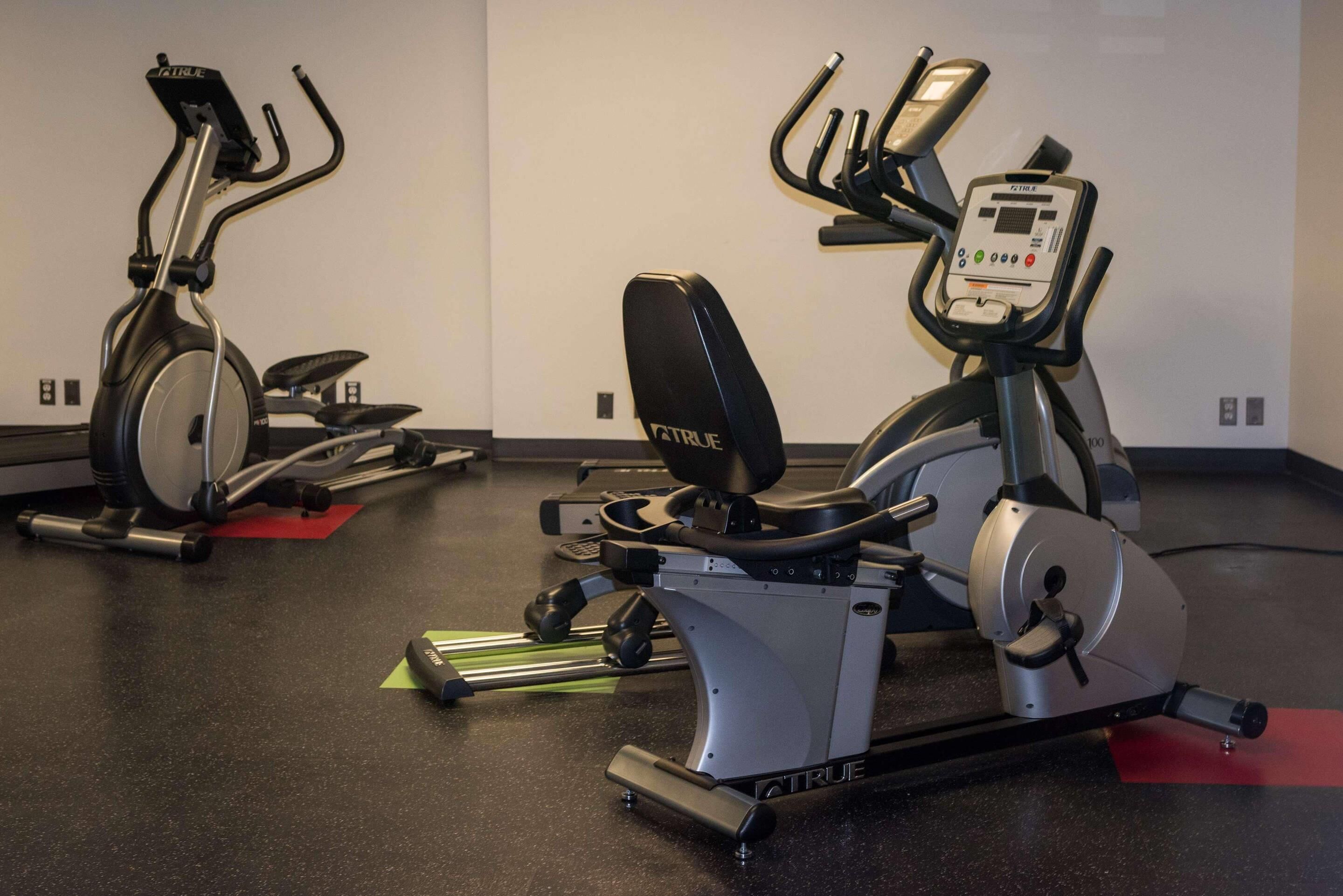 Dos bicicletas estáticas en un gimnasio con piso negro y paredes blancas.