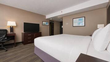 A hotel room with a bed, a desk with a television, a chair, and a door.