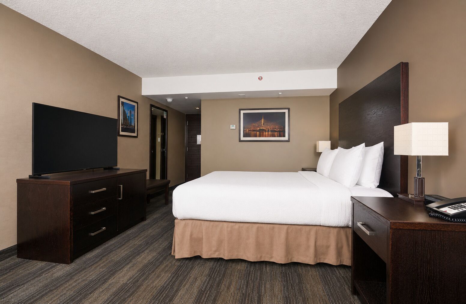 A hotel room with a bed, a desk with a lamp, a television, and a dresser.