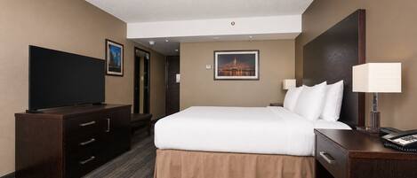 A hotel room with a bed, a desk with a lamp, a television, and a dresser.