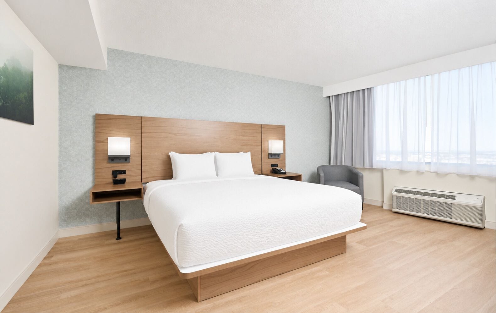 A modern hotel room with a large bed, bedside tables, a chair, and a window with curtains.
