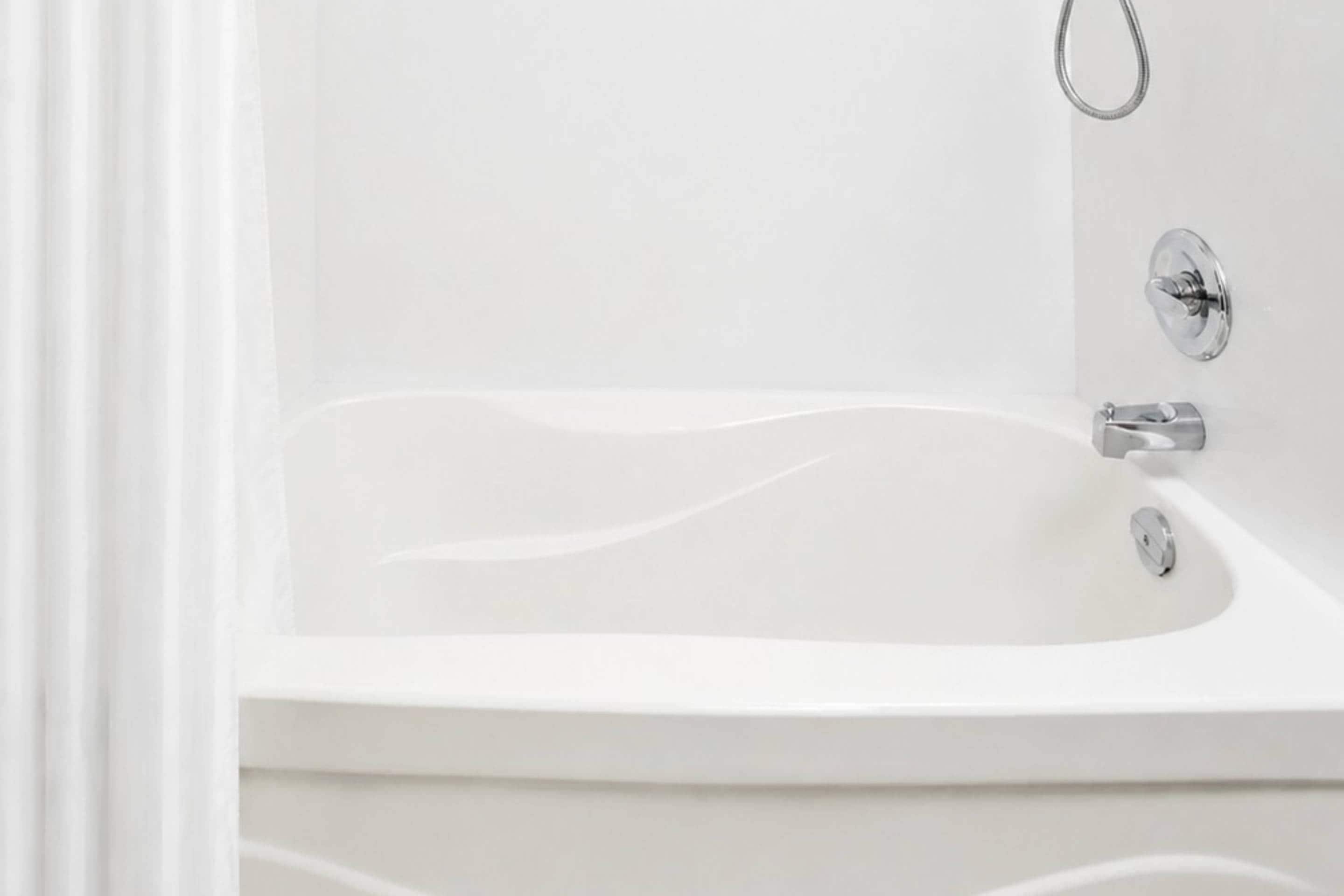 Una bañera blanca con grifo cromado y un mando circular.