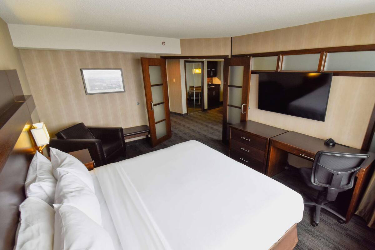 Ein Hotelzimmer mit einem großen Bett, einem Schreibtisch, einem Sessel, einem Fernseher und einer Tür zu einem Badezimmer.
