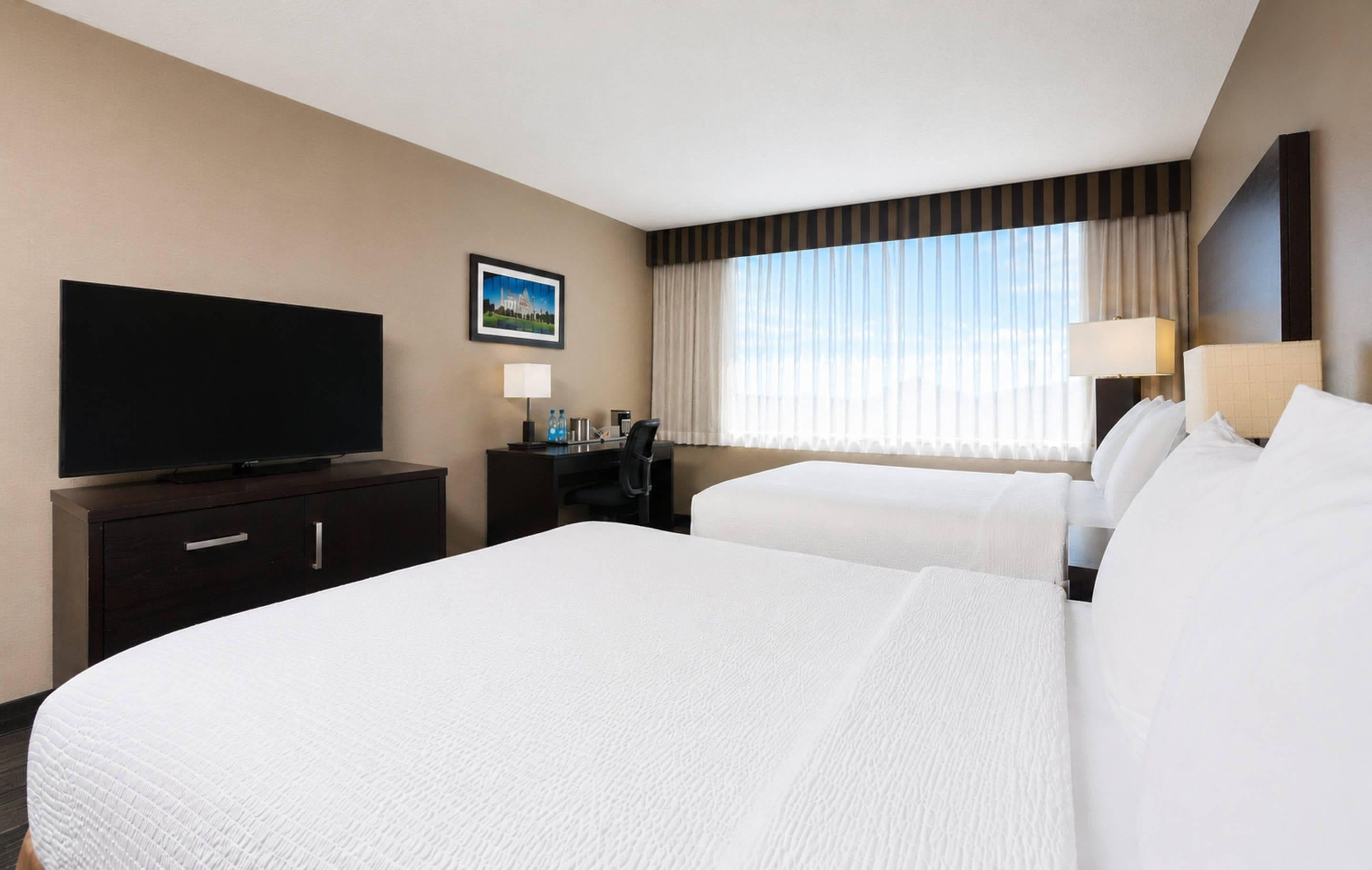 Habitación de hotel con dos camas, un escritorio, un televisor y una ventana con cortinas.