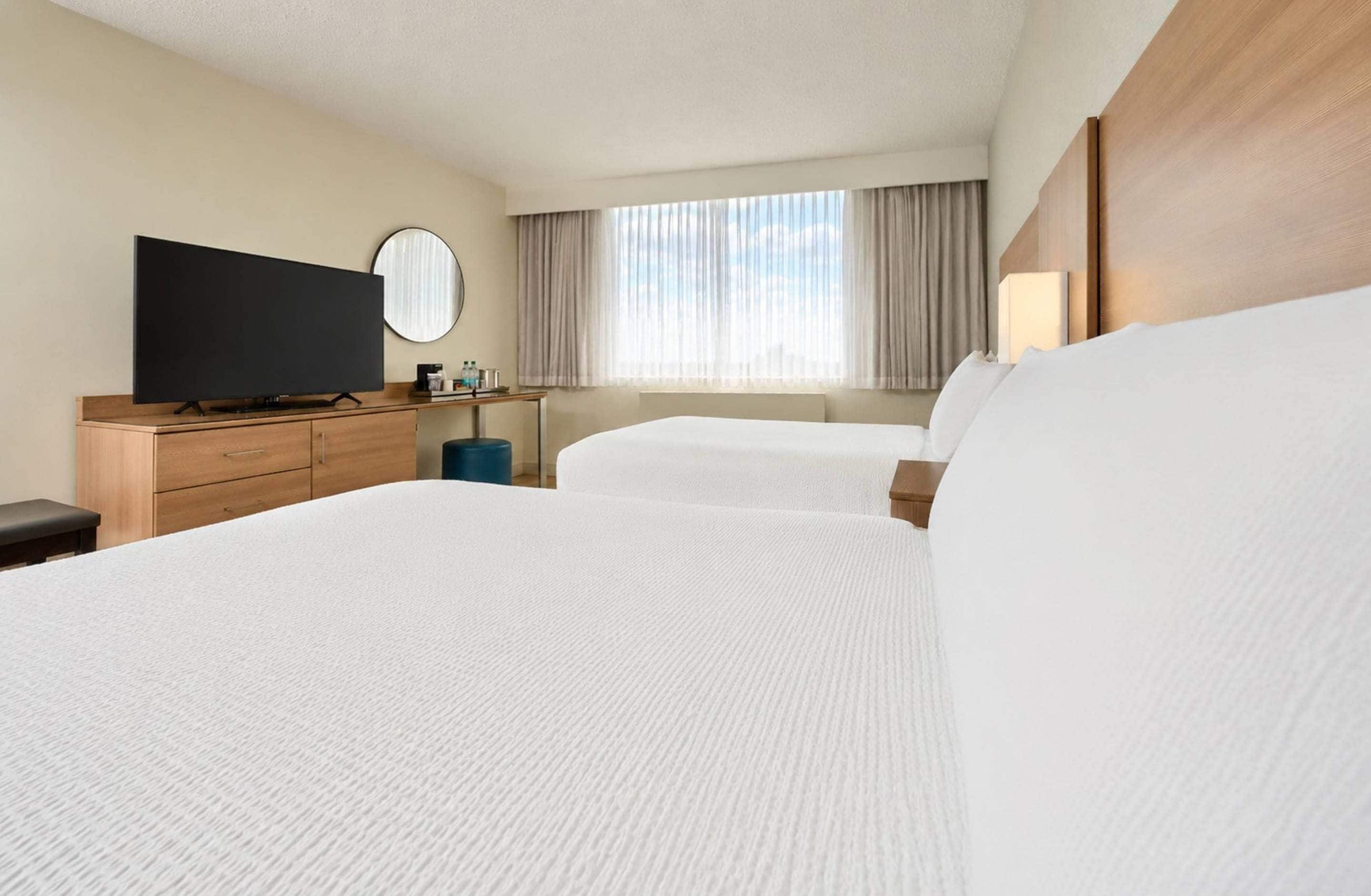 A hotel room with two beds, a television, a desk with a mirror, and a window with curtains.