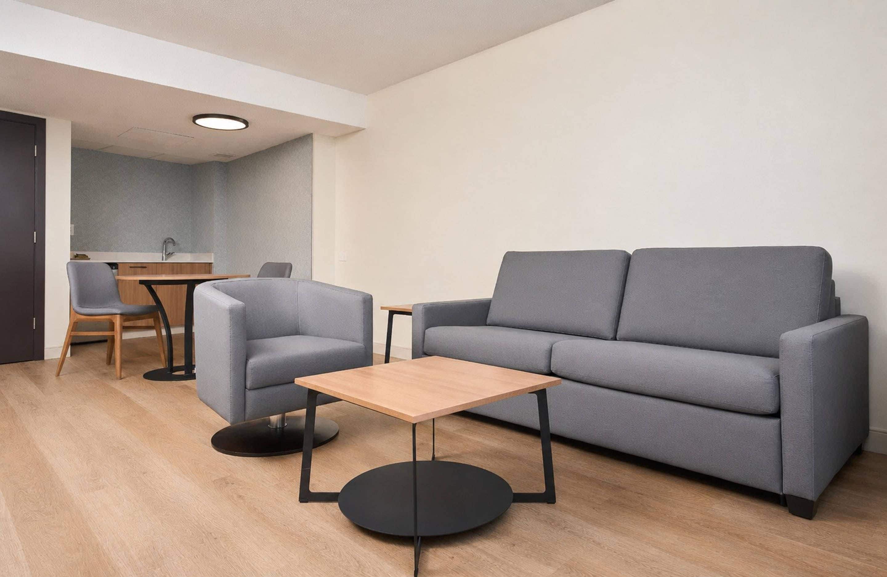 A modern living room with a grey sofa, a small wooden table, and a grey armchair.