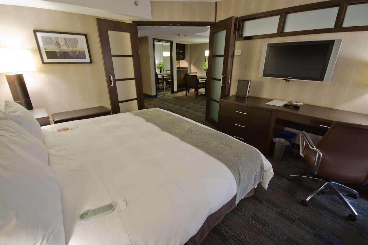 Ein Hotelzimmer mit einem großen Bett, einem Schreibtisch, einem Flachbildfernseher, einem Sessel und einem kleinen Tisch.