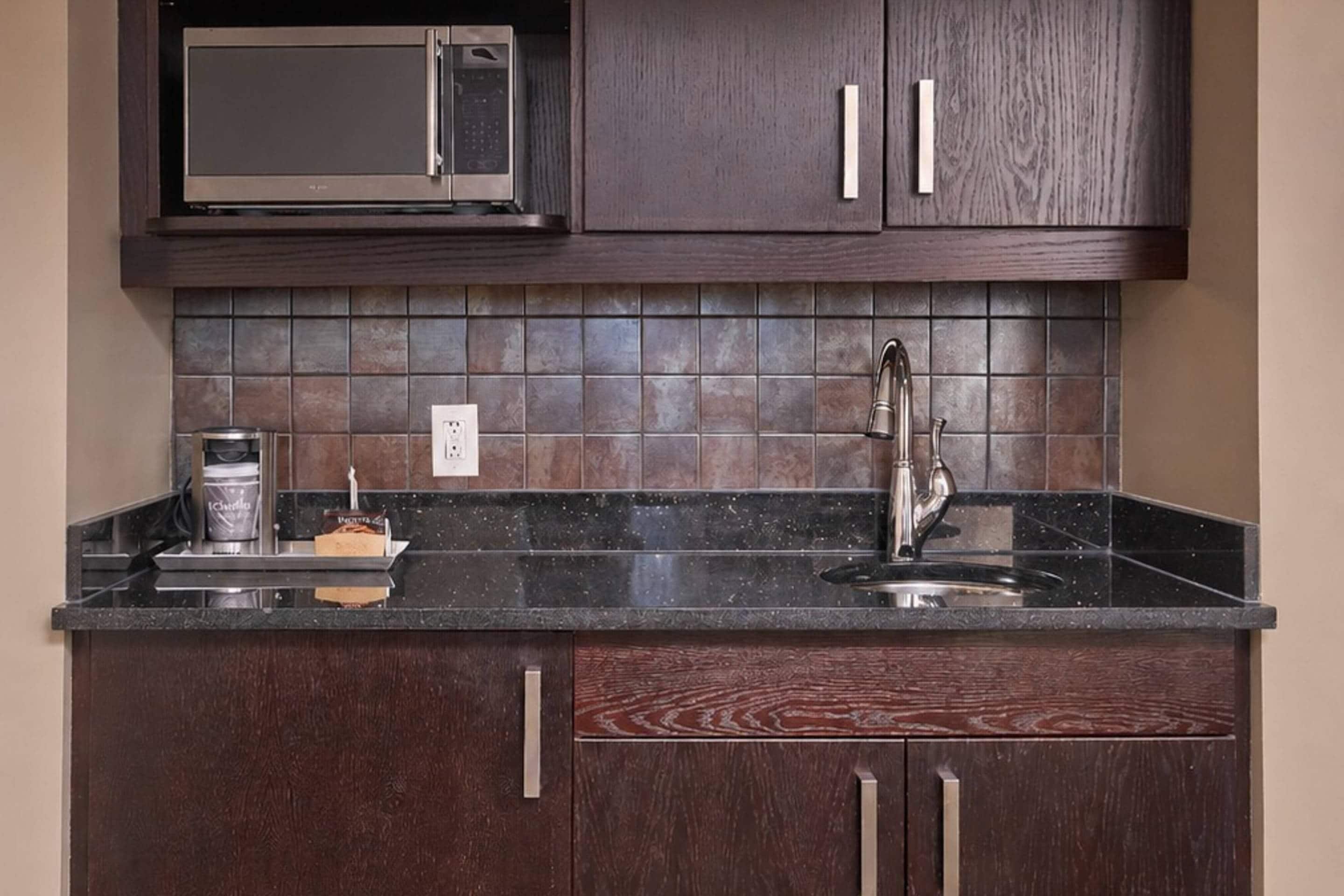 A kitchen with dark wood cabinets, a stainless steel sink, a microwave, and a coffee maker.