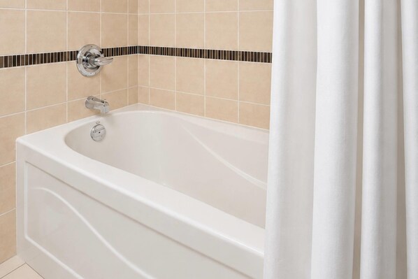 A white bathtub with a chrome faucet and a control knob, set against beige tiled walls with a black and beige border. - Radisson Hotel Winnipeg Downtown (Winnipeg)