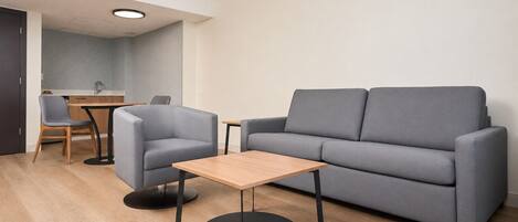 A modern living room with a grey sofa, a small round table, and a dining area with a wooden table and chairs.