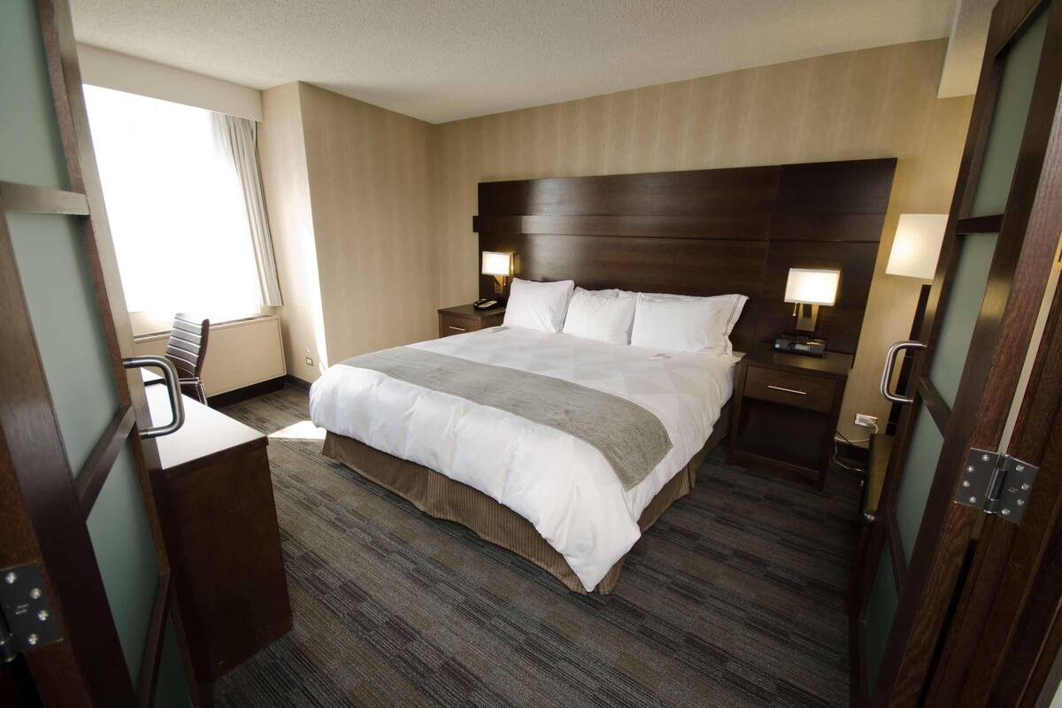 Ein Hotelzimmer mit einem großen Bett, zwei Nachttischen mit Lampen, einem Schreibtisch und einem Stuhl.